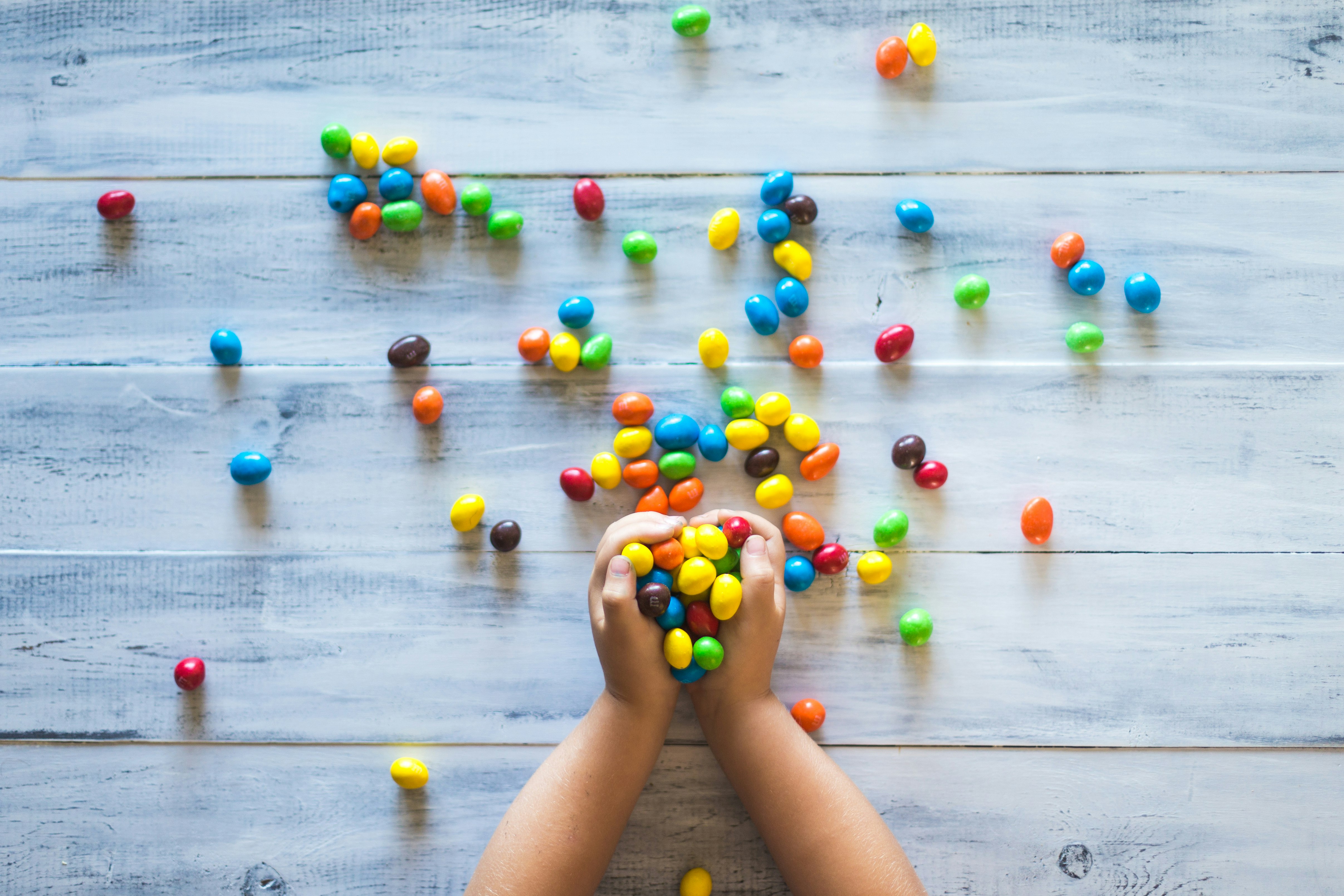 selective photo of kid holding candies on gray wooden pallet board